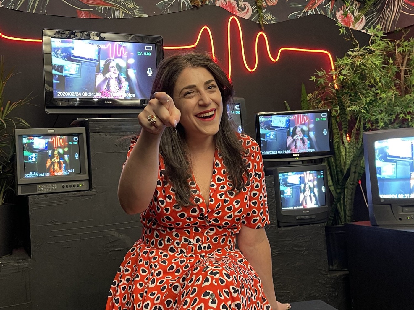Jessie pointing at the camera in front of a wall of monitors